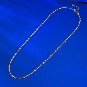 Detail of a gold-plated beaded necklace with lobster clasp on a blue silk background