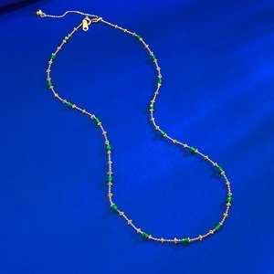 Macro shot of gold-plated beaded chain necklace with green crystals on royal blue background