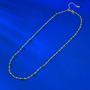 Detail of gold-plated chain featuring emerald green beads and a heart-shaped extension
