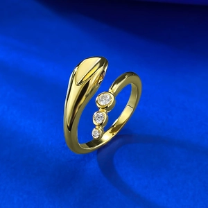 Macro shot of gold snake-shaped wrap ring with three vertical round zircons on blue background