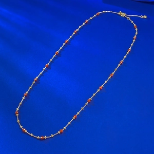 Close-up of golden necklace with red faceted beads and heart-shaped pendant detail