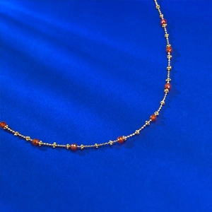 Detailed macro view of thin gold chain necklace with faceted red beads and gold beads