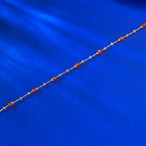 Close-up of a delicate gold chain bracelet with faceted garnet beads on blue silk