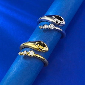 Macro shot of gold and silver snake-shaped open rings with crystals on blue background