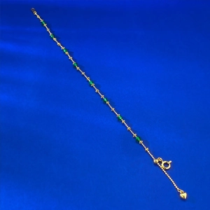 Detail of gold chain bracelet with green beads and a tiny heart pendant on blue silk