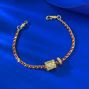 Dettaglio macro del bracciale in corda rossa con quadrifoglio dorato e anello di diamanti