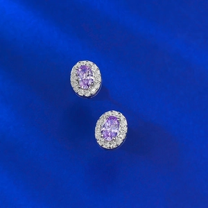 Elegant oval purple gemstone stud earrings with crystal halo on blue fabric background