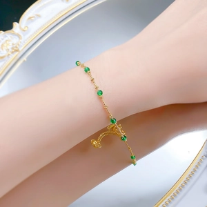 Close-up of a gold chain bracelet featuring small green beads and adjustable extender