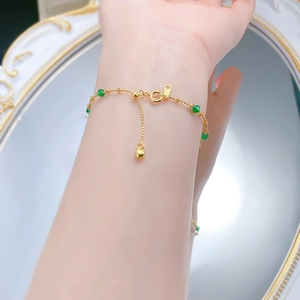 Detailed shot of a gold chain bracelet with green beads and a heart charm pendant