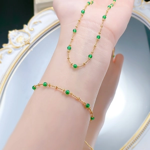 Close-up of gold chain bracelet with emerald green beads on wrist with vintage mirror