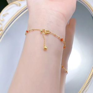 Detail of gold bead bracelet with red agate stones and heart charm on wrist
