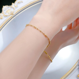 Close-up of a delicate gold beaded bracelet on a wrist against a vintage mirror
