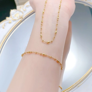 Detailed view of a gold beaded bar chain bracelet worn on wrist over a vintage mirror