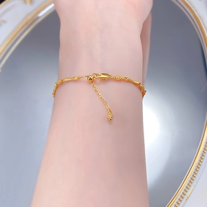 Detail of adjustable gold bamboo link bracelet with drawstring clasp and tassel charm