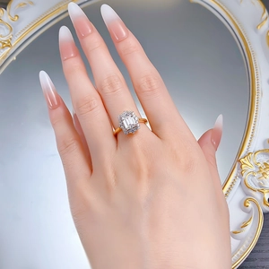 Detailed view of an emerald-cut ring with gold finish and halo small diamonds on a model hand