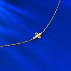 Elegant gold fleur-de-lis bracelet with brushed finish and zircon accents on blue fabric
