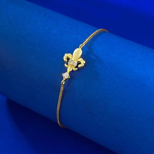 Elegant gold fleur-de-lis bracelet with crystal accents on a deep blue pedestal
