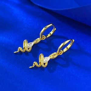 Macro shot of gold snake-shaped earring with marquise crystal on blue silk fabric