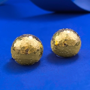 Macro shot of gold spherical earrings with detailed fish scale texture on dark background