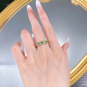 Close-up of gold ring with green and white gemstones on a model finger with a mirror