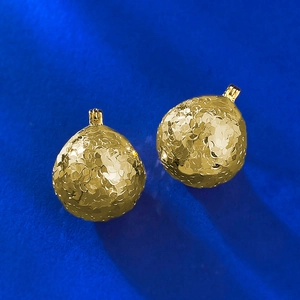 Macro detail of gold round drop earrings with floral relief on blue textured surface