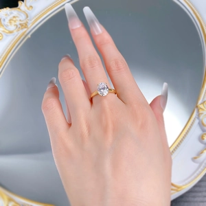 Detailed view of an oval white gemstone ring with a gold band worn on a finger