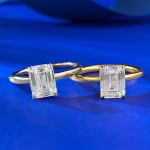 Detail of emerald cut gemstone rings in gold and silver finishes on blue fabric
