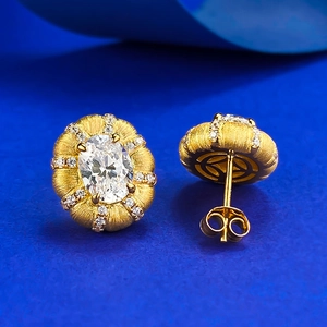 Close-up of gold earrings featuring brushed texture and oval zircon on blue background