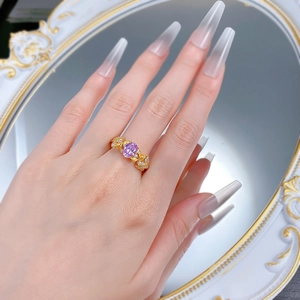 Détail d'une bague feuille dorée avec une pierre violette ovale au doigt