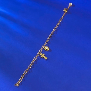 Dettaglio del bracciale dorato con croce e cristalli su sfondo blu testurizzato