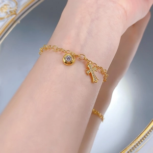 Dettaglio di un bracciale dorato con croce in zircone e ciondolo ad anello