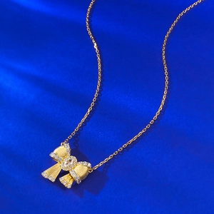 Close-up of golden bow pendant with brushed metal texture and sparkling zircon inlay