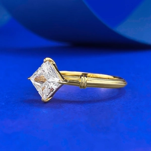 Bague solitaire en or taille princesse avec anneau nervuré sur fond bleu vif élégant