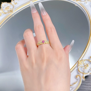 Detail of a wavy gold ring featuring a pink heart stone and side diamonds on hand