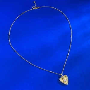 Macro detail of gold heart pendant with pink gem and woven mesh texture on blue silk