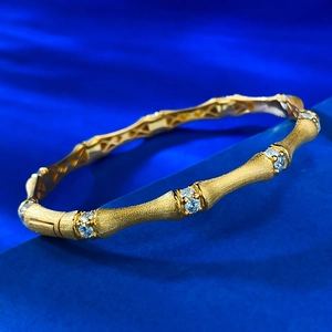 Detailed shot of a gold bamboo-style silver bangle with sparkling inlaid crystals on a blue stand