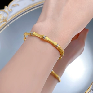 Detailed view of a gold bamboo-shaped bangle with frosted texture and white gemstones