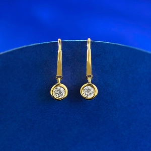 Macro view of gold hoop earrings featuring round white zircon drops on a blue stand