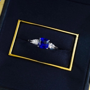 Close-up of a square-cut blue sapphire ring with teardrop side stones in a blue velvet box