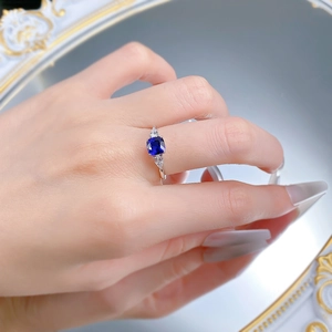 Close-up of a square cut blue sapphire ring on a hand over a reflective mirror surface