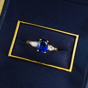 Macro detail of oval blue sapphire ring with side stones in a velvet jewelry box