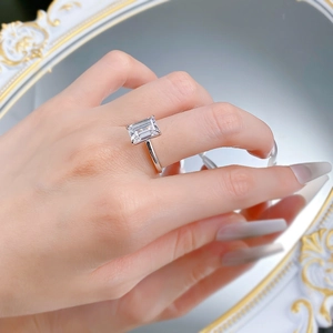 Detailansicht eines Rings mit Smaragdschliff am Finger vor elegantem Spiegelhintergrund
