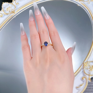 Top view of an elegant gold ring with a blue oval gemstone worn on a model's finger