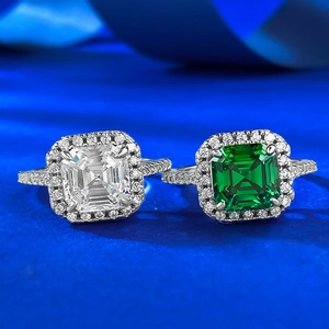 Detail of emerald cut green and white halo rings with pavé bands on blue silk