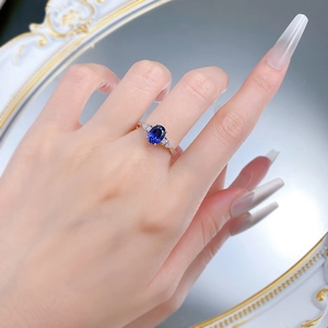 Close-up of S925 silver ring with oval blue sapphire and pear-shaped side stones on finger