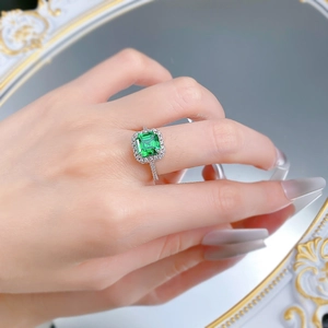 Detailed view of square emerald cut green gemstone halo ring on hand with mirror reflection