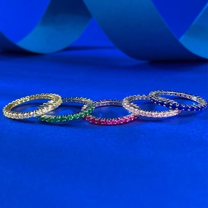 Five colored eternity rings with cubic zirconia stones displayed on blue background