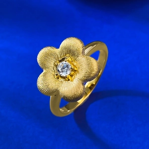Golden flower ring with brushed texture and sparkling center stone on blue background