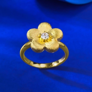 Macro detail of gold-plated flower ring with brushed petals and a sparkling zircon center