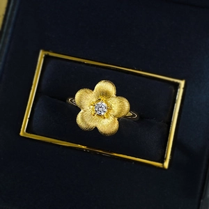 Golden brushed flower ring with sparkling center stone in a luxury blue jewelry box